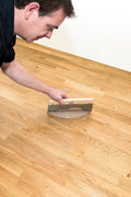 Osmo Double Blade Scraper spreading a thin coat of Osmo hardwax oil across an oak floor